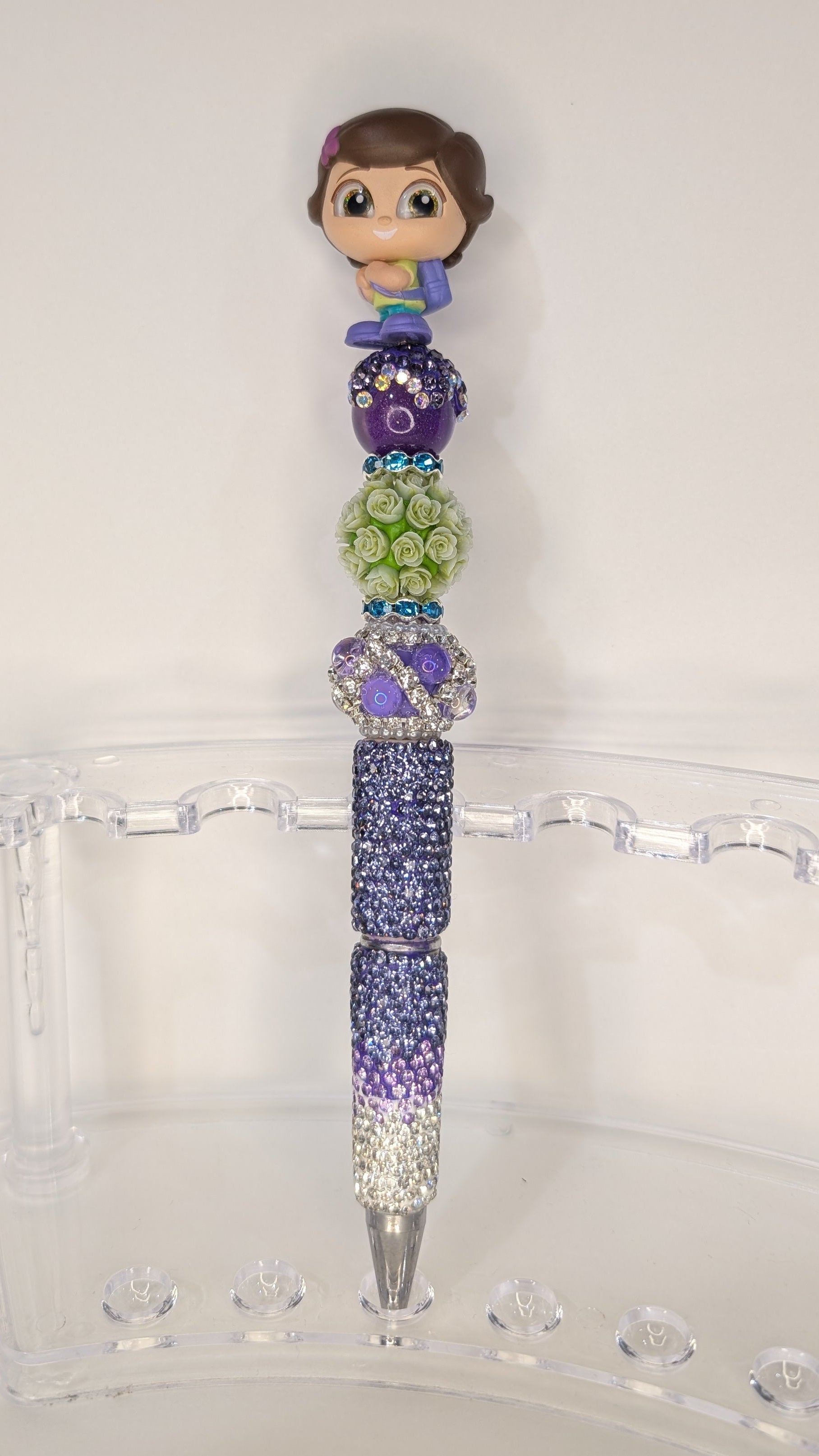 Decorative pen with colorful beads and a small figurine on top, placed on a clear stand.