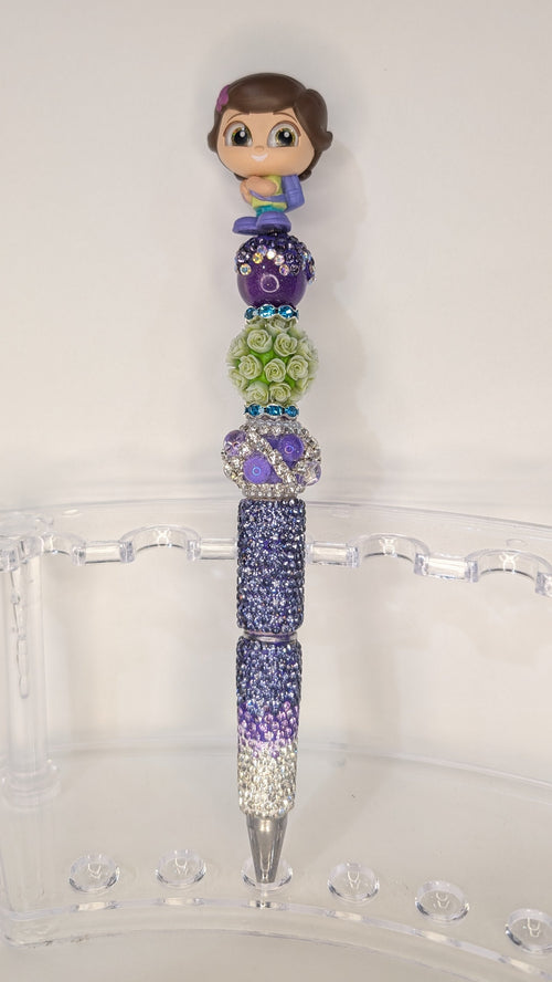 Decorative pen with colorful beads and a small figurine on top, placed on a clear stand.