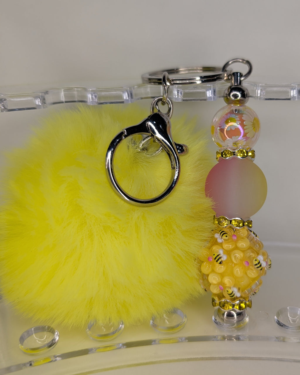 Yellow fluffy keychain with decorative beads on a clear stand.