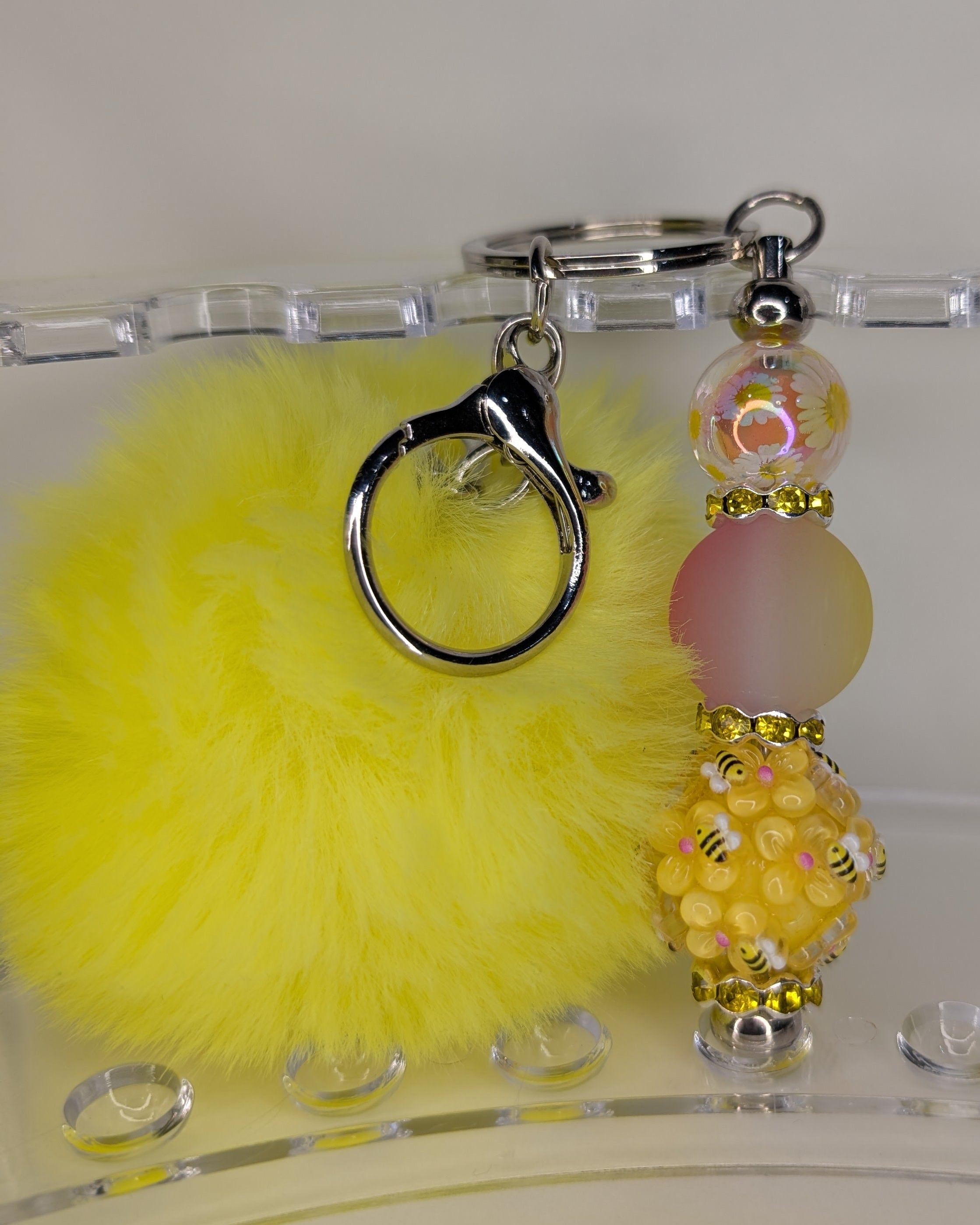 Yellow fluffy keychain with decorative beads on a clear stand.