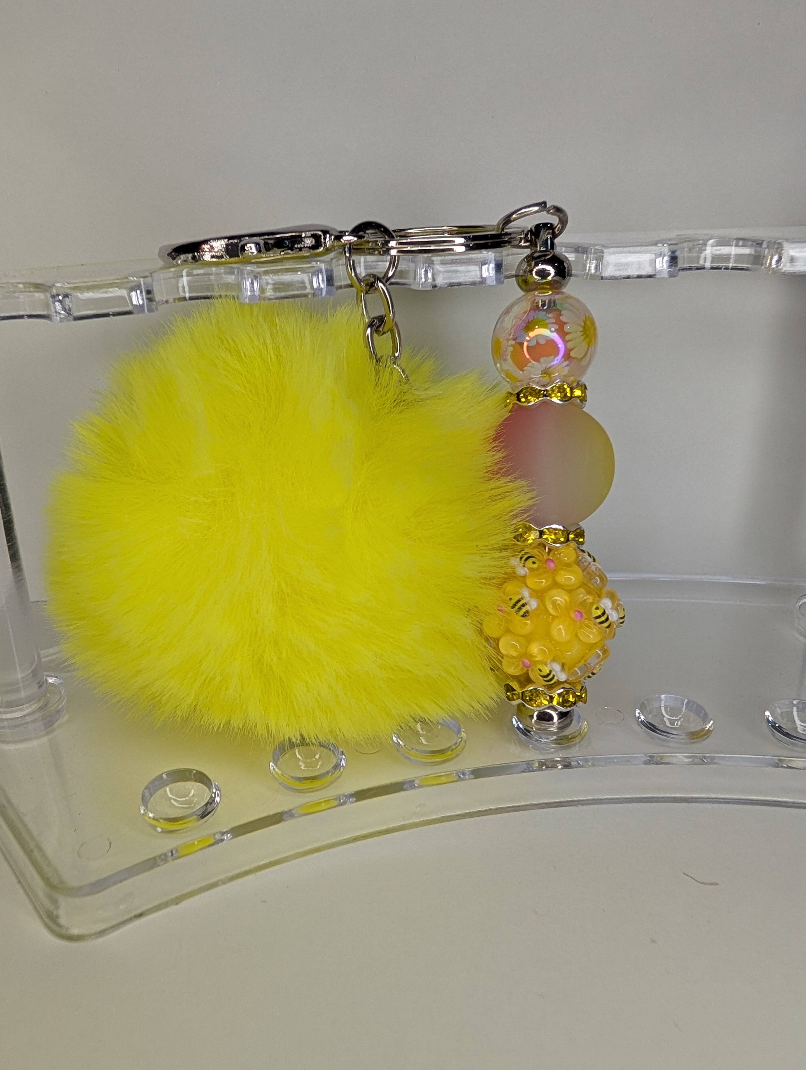 Keychain with yellow fluffy ball and decorative beads on a clear stand.