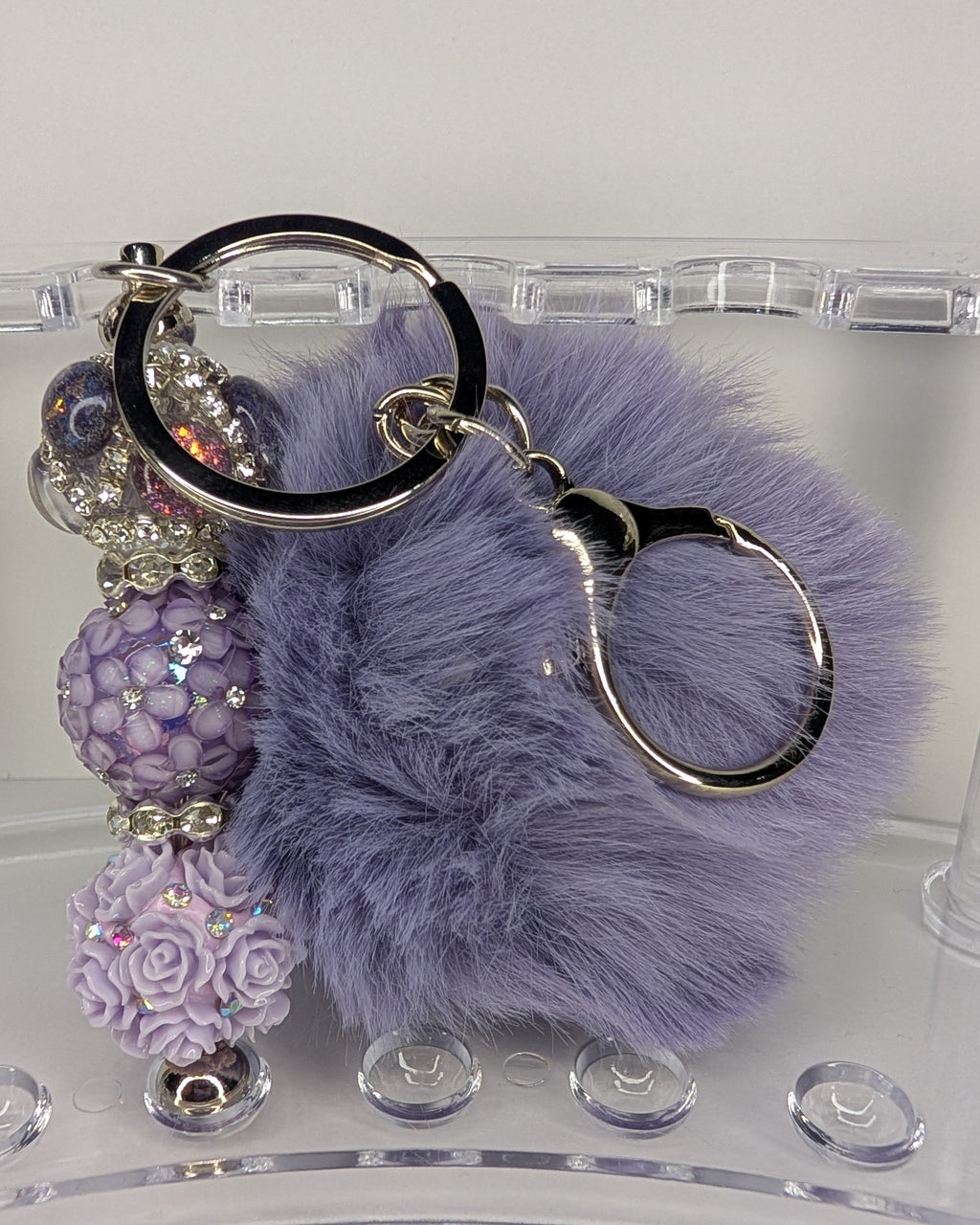 Purple fluffy keychain with decorative beads on a clear stand.