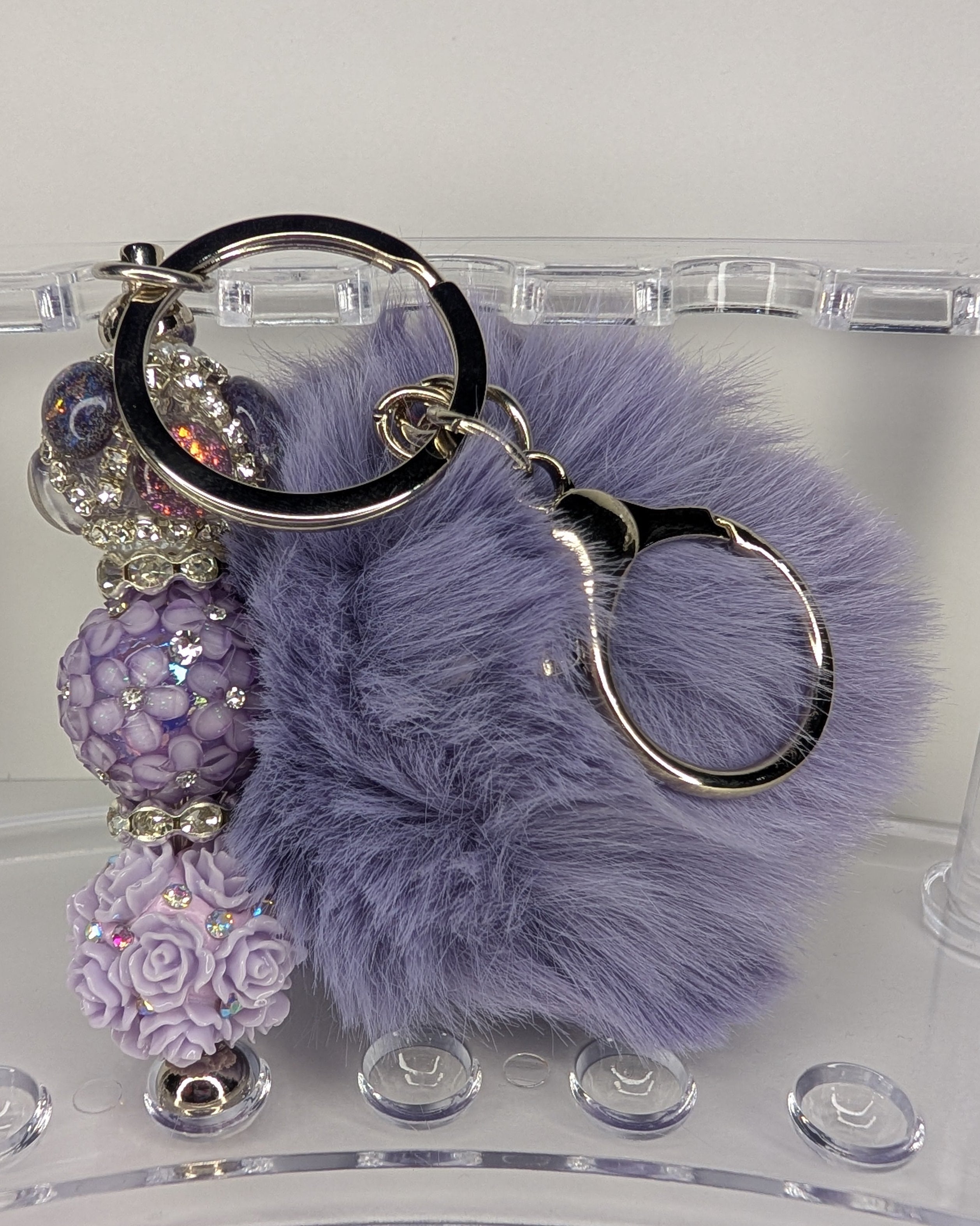 Purple fluffy keychain with decorative beads on a clear stand.