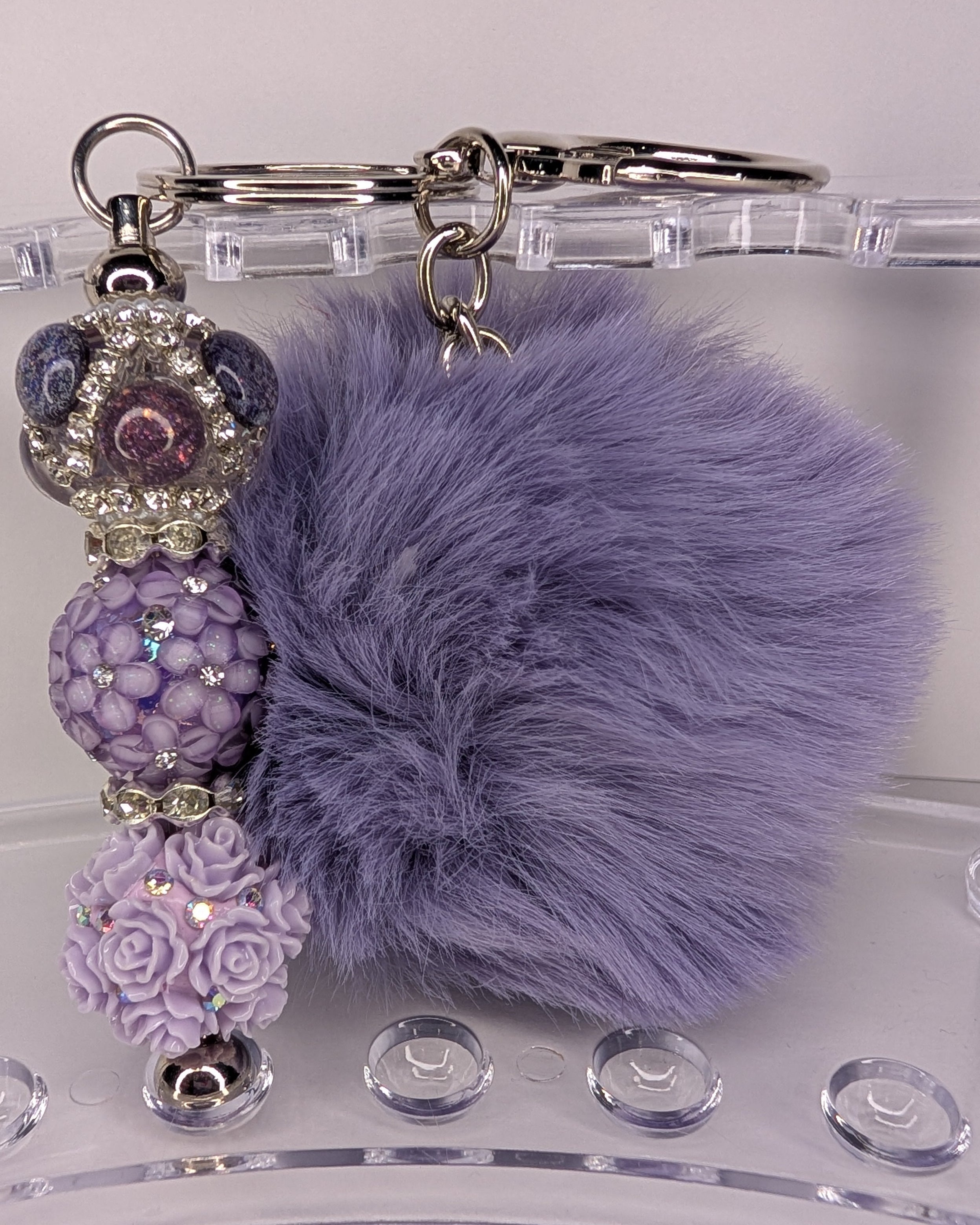 Purple pom-pom keychain with decorative beads on a clear stand.