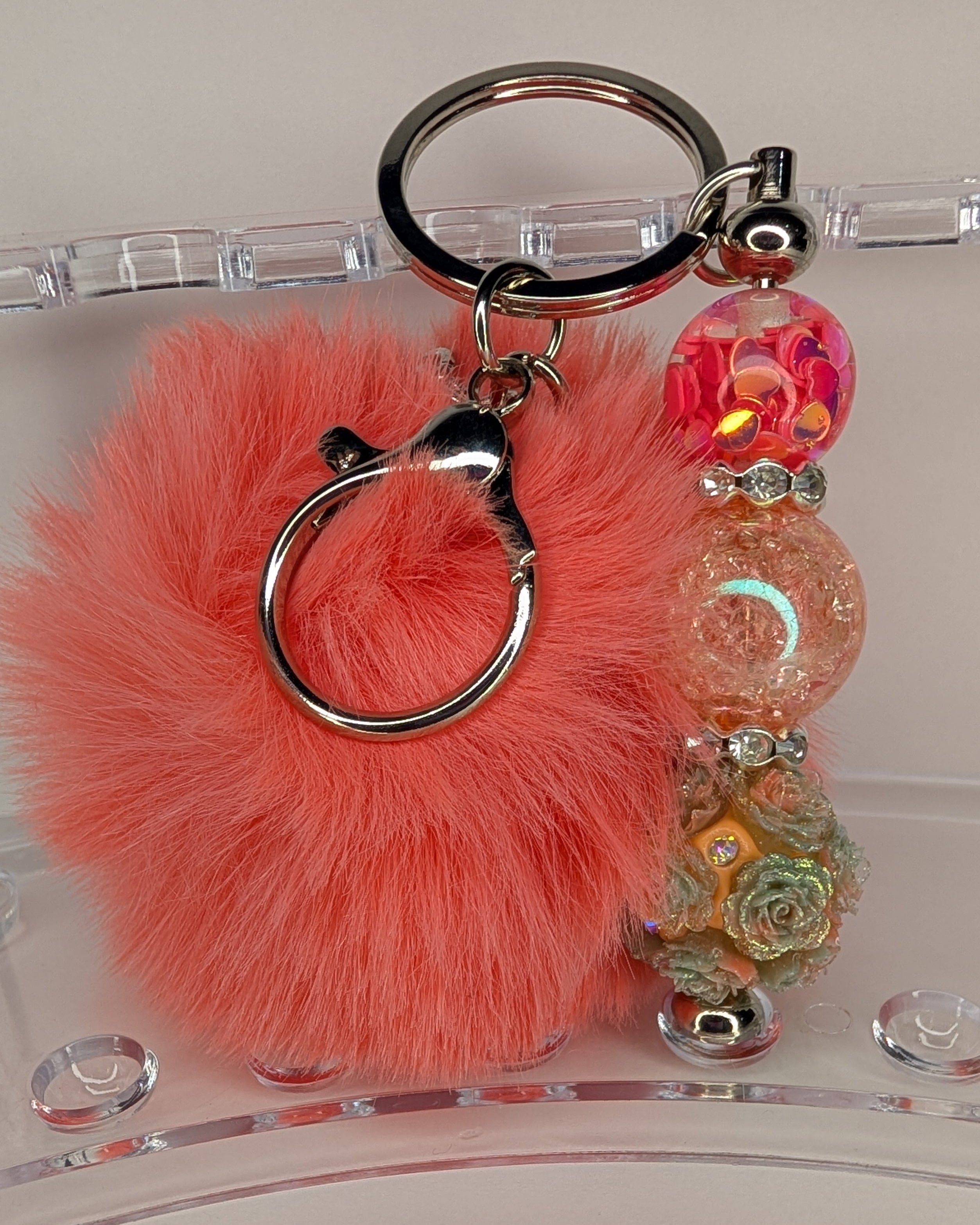 Keychain with pink fluffy ball and colorful beads on a clear stand.