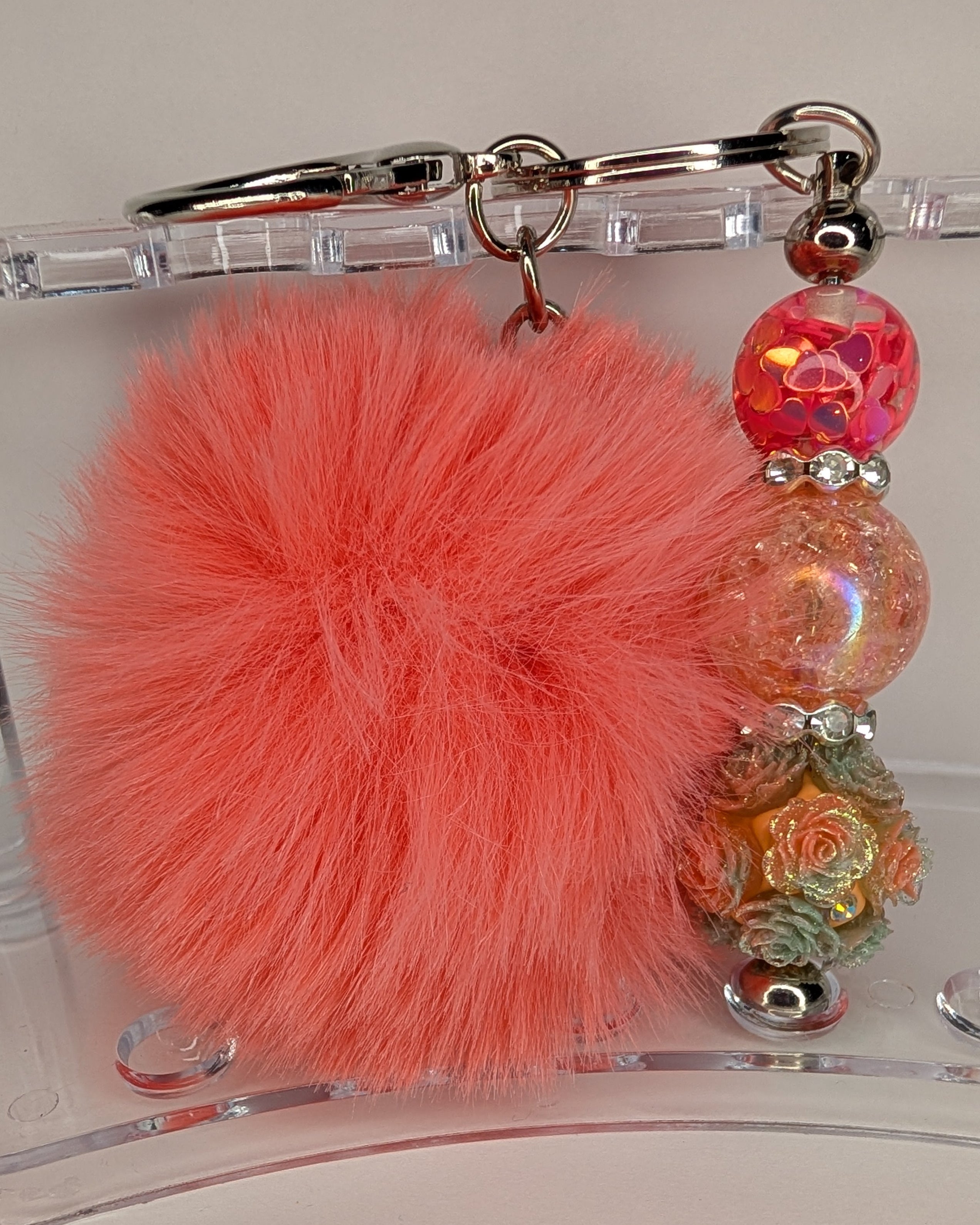 Keychain with pink pom-pom and colorful beads on a clear stand.