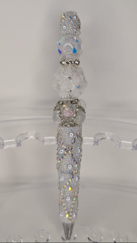 Decorative pen with gemstones on a clear stand against a white background