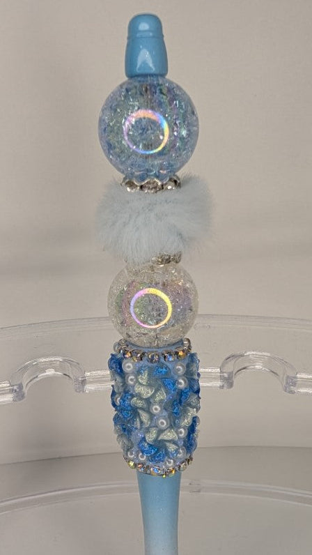 Decorative pen with blue and iridescent accents on a clear stand.
