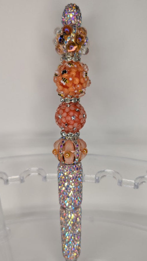 Decorative pen with multicolored beads on a clear stand against a white background