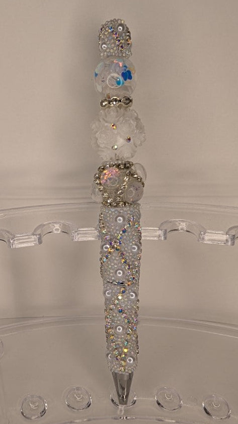 Decorative pen with gemstones on a clear stand against a neutral background