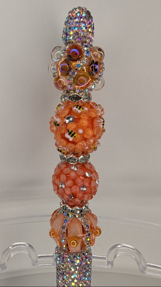 Decorative pen with orange flowers and gemstones on a clear stand against a light gray background