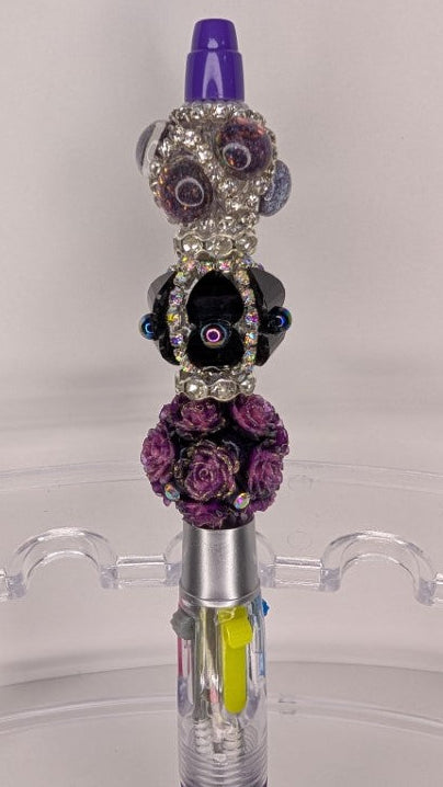 Decorative pen with purple accents and floral embellishments on a clear stand.
