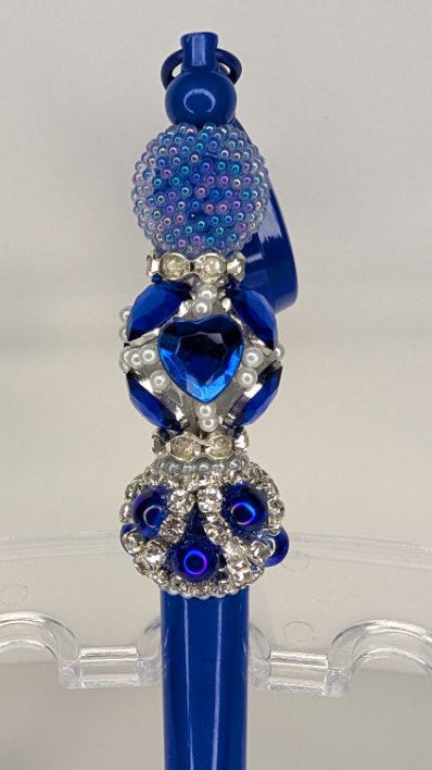 Decorative blue pen with embellishments on a clear stand against a white background