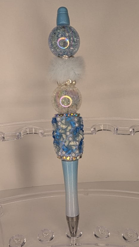 Decorative pen with blue and silver accents on a clear stand against a beige background
